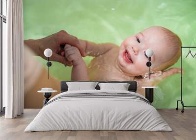 mom bathes the baby in the bathroom . the mother supports the head of the smiling child with her hand above the water Wall mural