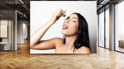 Young woman taking CBD or dietary supplement drops in mouth from dropper. Isolated. Close up shot. Wall mural