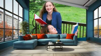 Two teenage girls reading books on bench in city park Wall mural