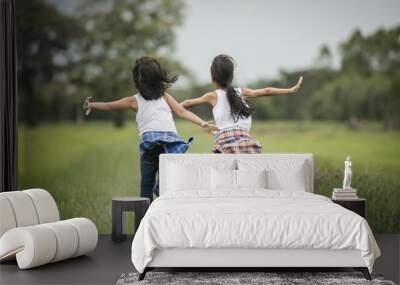 Two little cute girls are running on green grass. Best friends. Wall mural