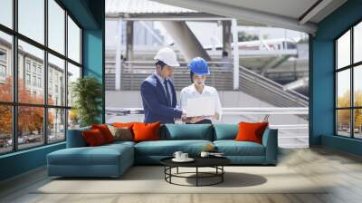 Two Asian engineers working or discussion on a building site and using laptop. Business people in safety helmet talk New Project or Product Details with Chief Engineering and architecture concept Wall mural