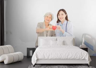 asian female doctor and old patient holding red heart with hands, happiness and relationship in hospital, they feeling happy and smile on white background Wall mural