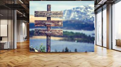 faith over fear text quote written on wooden signpost outdoors in nature with lake and mountain scenery in the background. Moody feeling. Wall mural