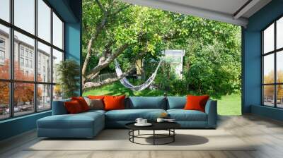 Hammock hanging in plum tree and greenhouse in lush green garden Wall mural