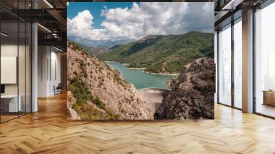 The dam wall at Lac de Tolla in Corsica surrounded by rocky cliffs and pine forest with mountains in the distance Wall mural