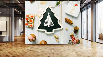 Christmas blackboard with a form of a christmas tree on a rustic background, christmas ornament atop of it, orange candieds, mistletoe ,cinnamon  sticks and a box with ho ho ho text greetings,top view Wall mural