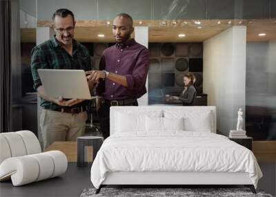 Diverse businessmen using a laptop while standing in a coworking office Wall mural