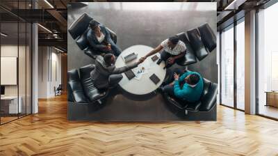 Group of African business people sitting and discussing statistics during a sit down meeting taking from above. Two colleagues are shaking hands Wall mural