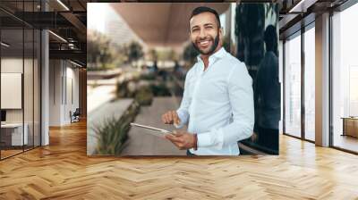 Portrait of a young confident smiling indian man holding a tablet and looking into the distance Wall mural