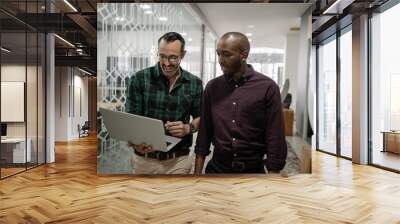 Two businessmen walking in an office an working on a laptop Wall mural