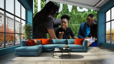 Two diverse African businesswoman talking with a group of work colleagues during a meeting together around a table in an office boardroom Wall mural