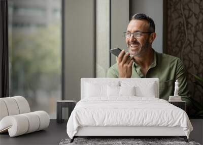 wide shot mature man with beard talking on phone next to sunny window Wall mural