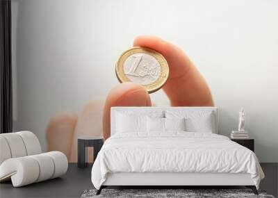 Closeup shot of adult male hand holding one Euro coin with two fingers on blur white background Wall mural