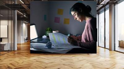 Student, reading notebook and studying at night with laptop of learning, education or internet project. Young woman, research paper and writing at dark desk for planning college homework in dormitory Wall mural