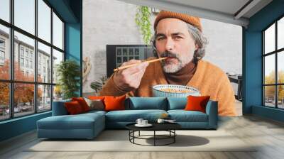 Mature Asian man with a white beard and long hair eating noodle dish with chopsticks Wall mural