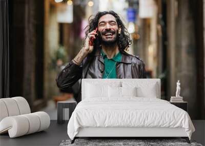 Stylish man wearing leather jacket is laughing while talking on the phone Wall mural