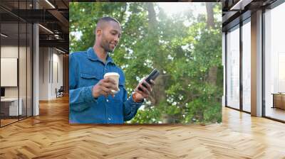 Park, texting and man relax with coffee, happy and calm in nature for travel, day off and tree background. Tea, black guy and online chat while standing in forest, casual and carefree on the weekend Wall mural