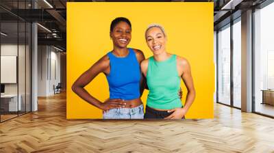 Portrait of a young cheerful female couple in front of a yellow background at studio. Two women together at studio. Wall mural