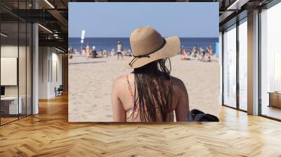 a woman with a hat on her head rests on the beach on the background of the sea and sand Wall mural