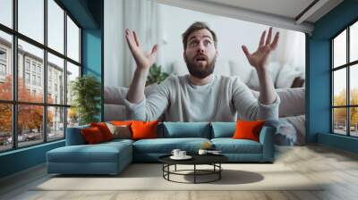 man sitting with arms raised with surprised expression sitting on sofa at home Wall mural