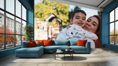 Loving embrace at the playground. Joyous mother hugs her autistic smiling young son at a sunny playground Wall mural