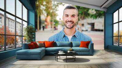 Close up portrait of handsome guy with perfect white teeth smiling and looking at camera standing outdoors. Front view of young man with friendly and positive expression. Happy adult male staring Wall mural