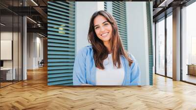 Happy caucasian young student female looking at camera enjoying with a perfect white teeth. Portrait of a joyful and adorable teenage brunette woman posing for a college promotion with crossed arms Wall mural