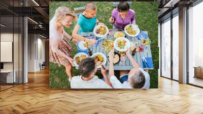 High angle view of adult friends sitting together at table, putting food on plates while having holiday dinner at backyard. High quality 4k slowmotion footage Wall mural