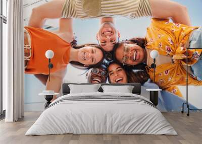 low view angle of a group of multiracial teenagers smiling and looking at camera together. Portrait of five young students smiling and laughing. Cheerful people having fun and embracing each others Wall mural