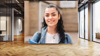 Pretty hispanic female student smiling and looking at camera in the high school. Head shot portrait of latin teenager girl standing outdoors at the university campus. Education concept. High quality Wall mural