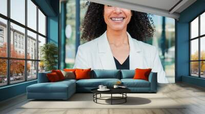 Vertical portrait of a hispanic arms crossed business woman with curly hair smiling looking at camera and standing at workspace wearing a suit. Folded corporate employee lady with successful attitude Wall mural