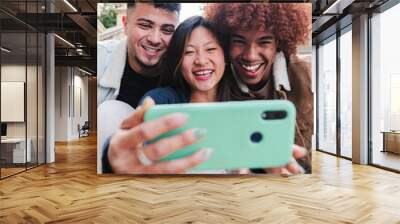 Vertical portrait of group of teenage multiracial friends having fun taking a selfie with a mobile phone. Young happy people smiling and watching funny videos or having a video call with a cellphone Wall mural