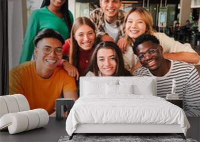 Vertical portrait. Group of young teenage students siting at library, using a laptop and looking at camera. Happy classmates studying and doing homeworks at high school. Multiracial academy people Wall mural