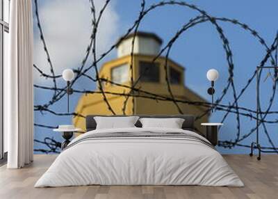 Guarding tower behind barbed wire fence stretched around prison walls Wall mural