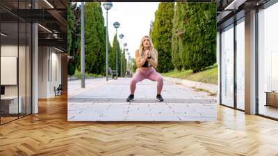 Fitness woman is performing squats in a park, wearing sportswear while training her legs and glutes Wall mural