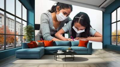 Latin mother helps her daughter with the homework on a black table at home, wears prevention mask. Teleworking and studying at home during coronavirus infection. Wall mural