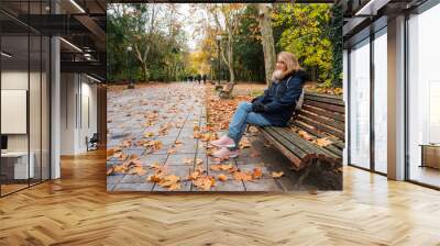 Woman sitting on a wooden bench in public park on a cold winter day. Wall mural