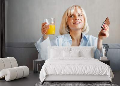 Close up pretty young woman holding a glass of orange juice and chocolate. Wall mural