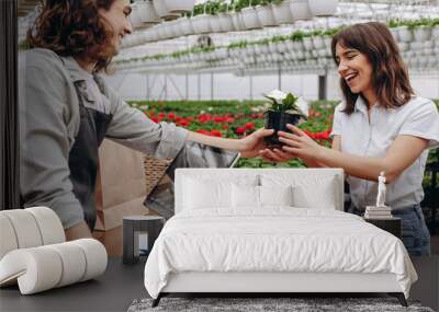 Photo of young woman buy flowerpot with florist man in greenhouse garden center. Wall mural