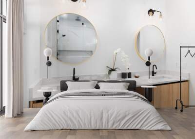 A bathroom with a floating white oak cabinet, white marble countertop, and black and gold lights over gold circular mirrors. Wall mural