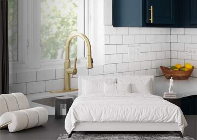 A kitchen detail with a gold faucet in front of a window, white subway tile backsplash, a bowl of fruit on the white marble countertop, and blue cabinets. Wall mural