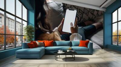 Looking over a woman's shoulder that's sitting on a couch in the evening and looking at her phone. The phone has a white screen to be able to add visuals. Wall mural