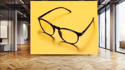 Close up photograph of a pair of light filtering reading glasses or spectacles with black modern minimalistic plastic frames on a bright yellow background. Wall mural