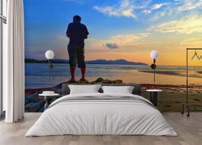 A beautiful sunset with a man standing on stony rocks background. Wall mural