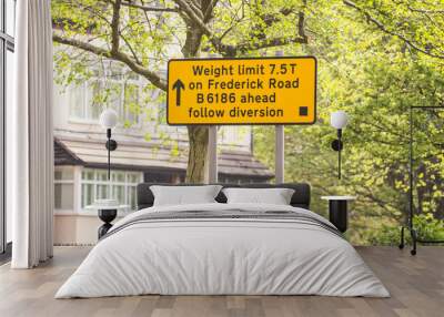 Yellow road sign in England showing the weight limit of 7.5 T on frederick road, also highlighting the B 6186 diversion in front of an urban background including trees and nature Wall mural