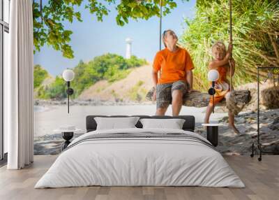 Mother and daughter on rope swing under palm trees on tropical b Wall mural