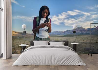 athletic african american woman with backpack looking at smart phone while hiking in red rock canyon Wall mural