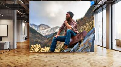 happy bearded guy sitting on luggage at top of mountain Wall mural