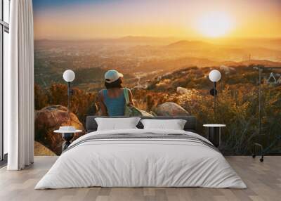 Rear view of woman hiker sitting on rock on top of hill while looking at sunset over San Diego California Wall mural