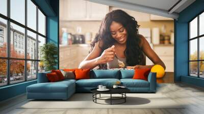 Smiling young woman eating breakfast at table in kitchen Wall mural